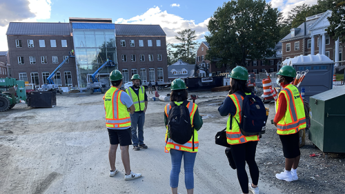 Group of students in high visibility vests stand in front of the Irving building under construction